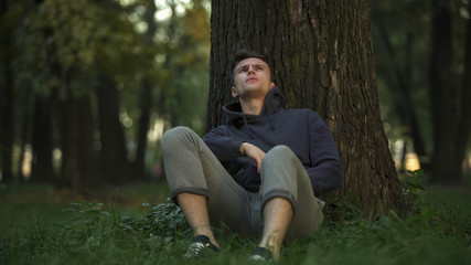 Depressed man sitting under tree in park, unemployment problem, difficulties