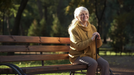 Happy aged woman enjoying warm sunny day sitting on bench in park, retirement