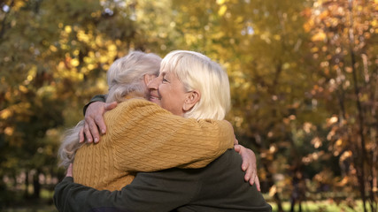 Senior female friends hugging and meeting in autumn park, friendship through age