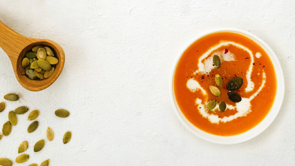 Roasted pumpkin soup with cream and pumpkin seeds and wooden spoon on white background. Copy...