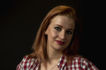 Fototapeta premium Low key portrait of happy young woman dressed in a plaid shirt. All is on the black background. 