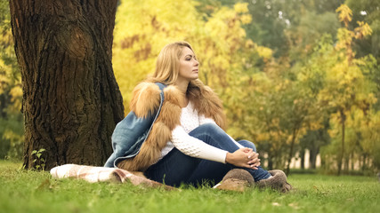 Pensive woman enjoying beautiful weather in autumn central park, yellow leaves