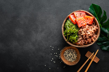 Poke bowl with raw salmon fish, chuka salad and rice in coconut bowls on black background