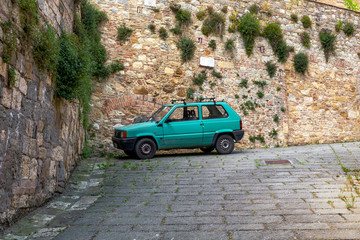 Old retro car parked in the corner, in front of the medieval brick wall on the street of the old town in Italy.