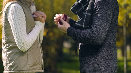 Man with engagement ring asking woman to marry him in autumn park, surprise