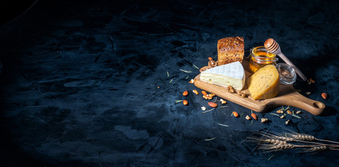 Different kinds of cheese with nuts and honey on dark background, copy space