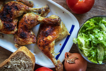 Roasted chicken legs with salad and bread on wooden table
