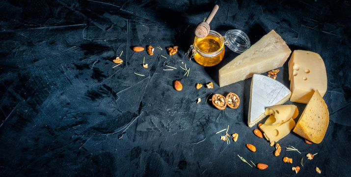 Different kinds of cheese with nuts and honey on dark background, copy space