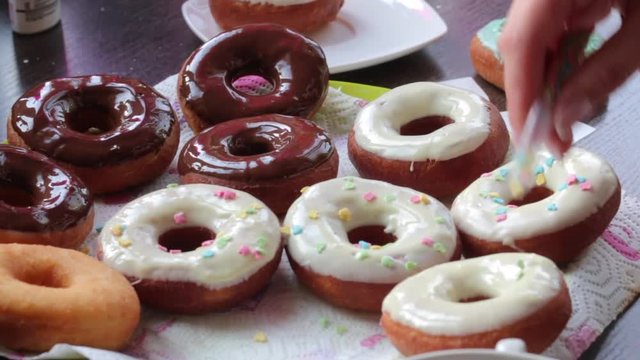 A woman decorates with dressing American donuts glazed with melted chocolate.