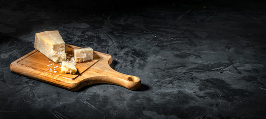 Piece of Parmesan cheese on dark background, copy space