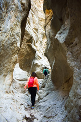 hiker with a backpack climbing a defile. Woman hiker between two white stone walls made by a dry river that has transformed this valley into a defile