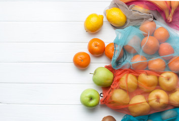 Fruits in eco-friendly shopping bags on white wooden background with copy space