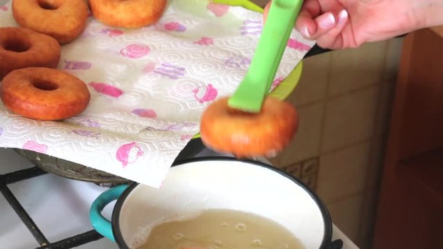 A woman is cooking American donuts. Bake them in sunflower oil. Nearby are cooked donuts..