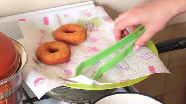A woman is cooking American donuts. Bake them in sunflower oil. Nearby are cooked donuts.