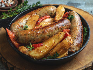 grilled chicken sausages with fried potatoes and peppers in an iron pan