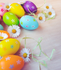 Close up and top view of colorful painted easter eggs decoration with fresh white blooming daisies on wooden background. Happy Easter background