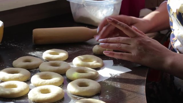 A woman makes blanks for American donuts. Made of dough, lie on the surface of the table. Nearby are tools for cooking...