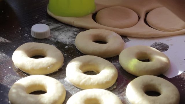 A woman makes blanks for American donuts. Made of dough, lie on the surface of the table. Nearby are tools for cooking.