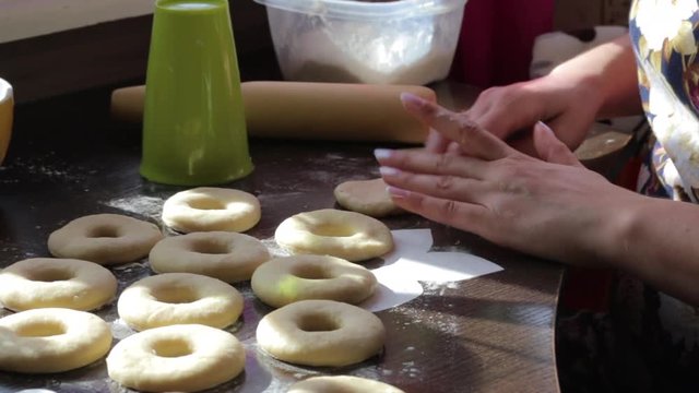 A woman makes blanks for American donuts. Made of dough, lie on the surface of the table. Nearby are tools for cooking_