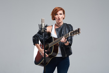Portrait of a young woman musician with an acoustic guitar. Sing a song on studio microphone on a...