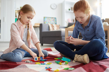 Fototapeta premium Full length portrait of two sisters playing with puzzles sitting on floor at home, copy space