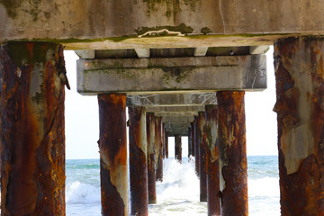 Under a fishing pier looking out into the ocean with waves present