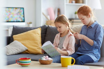 Portrait of two sisters braiding hair enjoying leisure time together at home, copy space