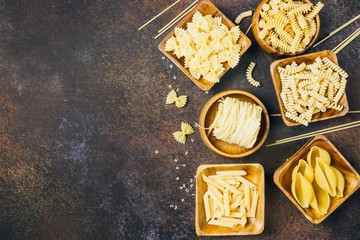 Various pasta on wooden bowls over dark background