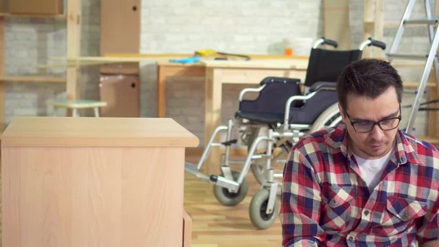 Portrait of a young disabled man next to a wheelchair collects a bedside table