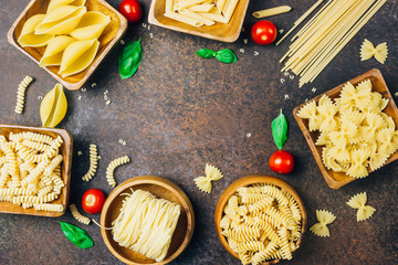 Various pasta on wooden bowls over dark background