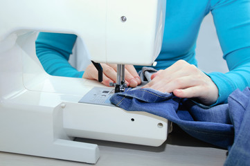 Caucasian girl sews denim on the sewing machine. Close-up.