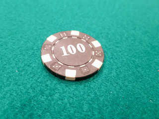 a black poker chip of 100 on a green game mat
