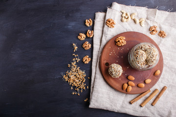 Energy balls cakes with almonds, sesame, cashew, walnuts, dates and germinated wheat in glass jar, top view, black background.