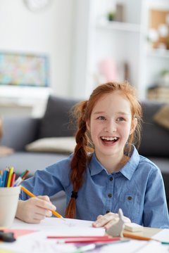 Portrait of excited red haired girl drawing pictures sitting at table at home, copy space