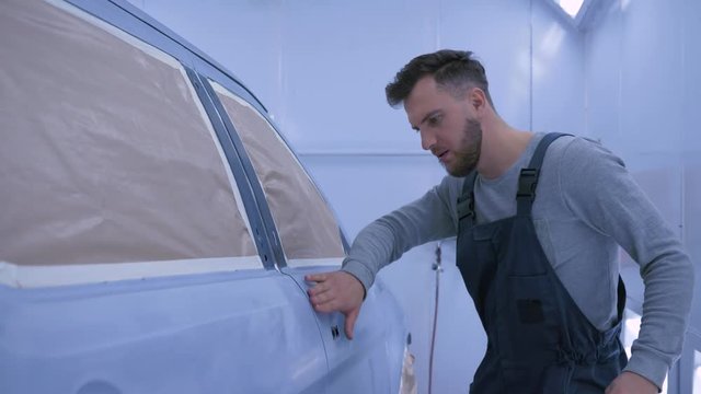 professional Auto painter guy sanding car after paint by hand at paint chamber during repair work at service station
