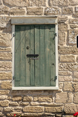 A green plank wooden door with a white frame set against a stone house