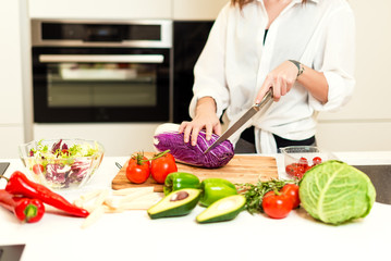 Brunette woman on the kitchen cutting cabbage andpreparing healthy nutrition salad from fruits and vegetables. Housewife concept