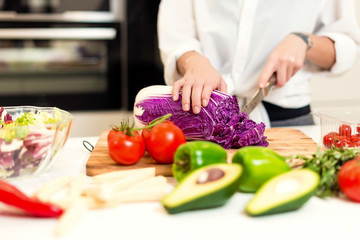 Brunette woman on the kitchen cutting cabbage andpreparing healthy nutrition salad from fruits and vegetables. Housewife concept