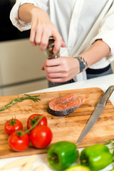 Brunette woman preparing fresh fish steak on the kitchen with vegetables and glass of white wine. Housewife concept