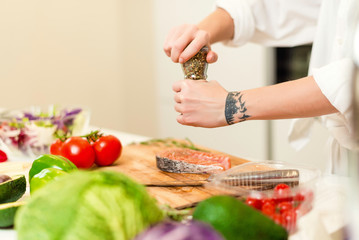Brunette woman preparing fresh fish steak on the kitchen with vegetables and glass of white wine. Housewife concept