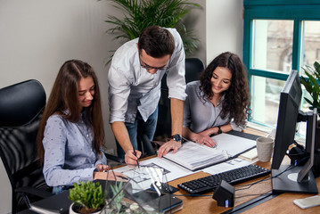 Handsome firm manager in glasses explains work tasks for his employees. Creative people or advertising business concept. Team work. Young beautiful people working in office together.