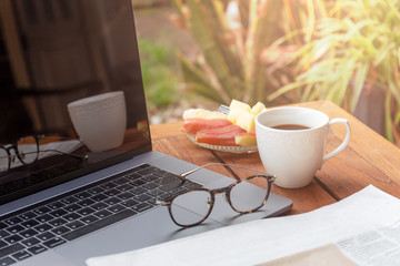Laptop computer with coffee mug and news paper on table.