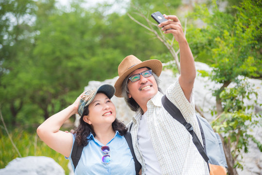 Happy asian retired couple taking their photo by smart phone while hiking in mountain