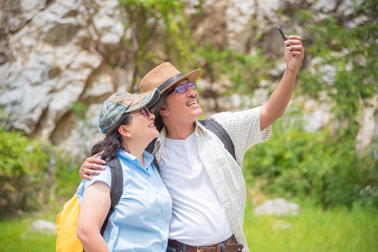 Happy asian retired couple taking their photo by smart phone while hiking in mountain