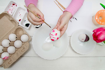 Obraz na płótnie Canvas A flat lay with kid's hands painting Easter eggs on white wooden table
