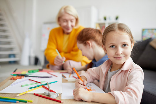 Portrait of cute little girl looking at camera while drawing pictures at home with family, copy space