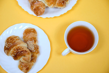 croissants on a white plate with a Cup of tea on a yellow background