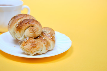 croissants on a white plate with a Cup of tea on a yellow background