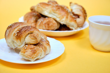 croissants on a white plate with a Cup of tea on a yellow background