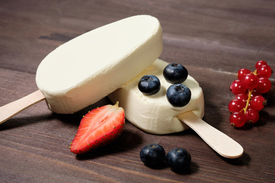 white cream ice cream on a stick with strawberries, blueberries and red currants on the dack wood background
